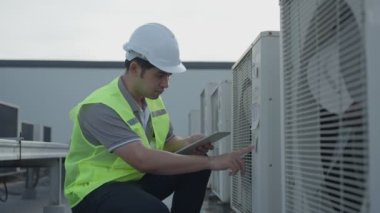 asian maintenance engineer works on the roof of factory. contractor inspect compressor system and plans installation of air condition systems in construction. technology, online checking, mobile app