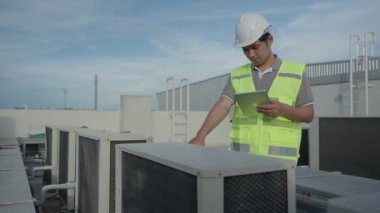 Asian maintenance engineer works on the roof of factory. contractor inspect compressor system and plans installation of air condition systems in construction. technology, online checking, mobile app.