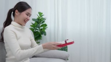 Güzel Asyalı kadın şaşırır ve hediye kutusuyla ilgilenir. Sevimli kız hediye kutusunu açtı. Doğum günü, kutlama, xmas, yeni yıl festivali, teşekkür, kutlama, sevgililer günü, yıldönümü