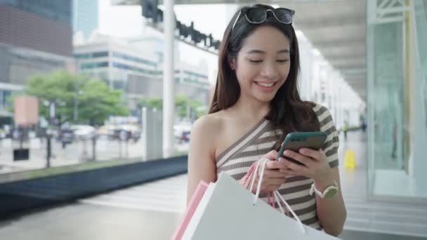 现代快乐的亚洲女性生活时尚肖像 漂亮迷人的年轻女子喜欢带着购物袋散步 街上用的是智能手机 商场里穿的是时髦的衣服 — 图库视频影像