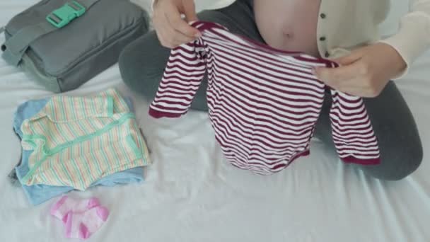 妊娠中の女性は子供の準備のために注文して掃除した後に服を畳んでいます 新しい父と母のためのベビー服アクセサリーを準備するためのアイデア — ストック動画