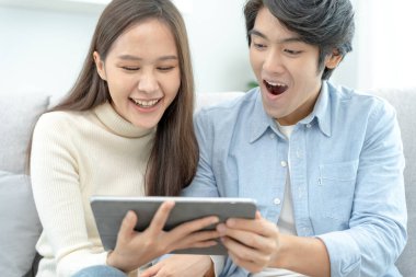 Gülümseyen Asyalı çift internet alışverişinde akıllı telefon kullanıyor. Koca, güzel bir eş için doğum günü hediyesi ödemeye hazır. Balayı için internetten konaklama, uygulama, uçak biletleri..