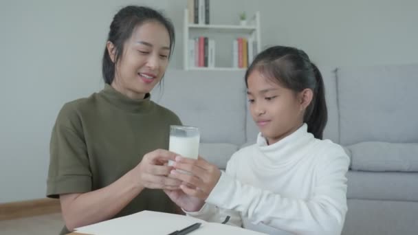 アジア系の少女は家で学ぶ 親切な母親の助けを借りて宿題をし 試験を奨励してください 母さんは娘に牛乳を１杯渡す 女の子幸せな家庭学校 母は教育と助言を共にする — ストック動画