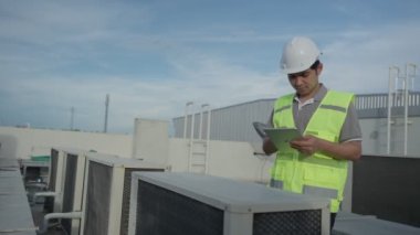 Asian maintenance engineer works on the roof of factory. contractor inspect compressor system and plans installation of air condition systems in construction. technology, online checking, mobile application.