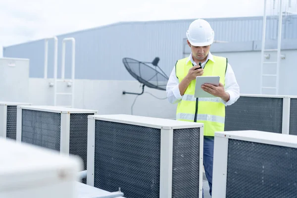 Asian maintenance engineer works on the roof of factory. contractor inspect compressor system and plans installation of air condition systems in construction. technology, online checking, mobile application.