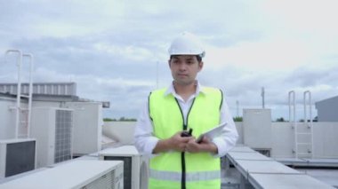 Asian maintenance engineer works on the roof of factory. contractor inspect compressor system and plans installation of air condition systems in construction. technology, online checking, mobile application.