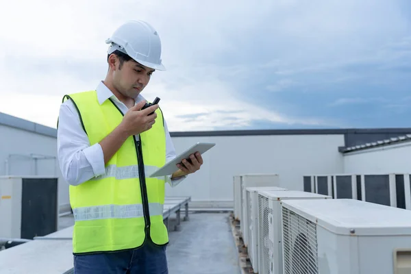 Asian maintenance engineer works on the roof of factory. contractor inspect compressor system and plans installation of air condition systems in construction. technology, online checking, mobile application.