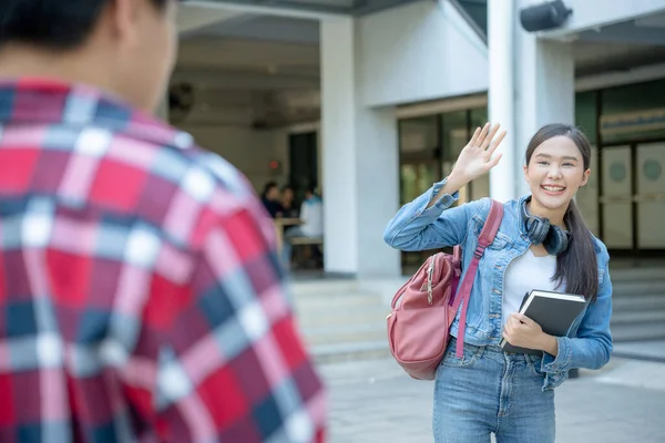 Beautiful student woman with backpack and books outdoor is greeting friends. Smile girl happy carrying a lot of book in college campus. Portrait female on international Asia University. Education