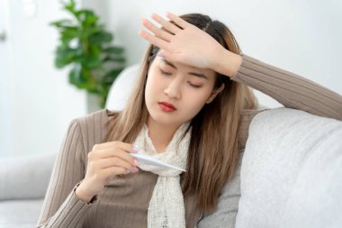 Young Asian woman having high fever while checking body temperature, female sneezing and runny nose with seasonal influenza, allergic, digital thermometer, virus, coronavirus, illness, respiratory