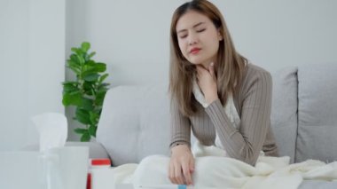 Asyalı kadın boğazı ağrıdığı için elini boynuna koydu. Dişi bademcik iltihabı iltihaba neden olur. Su alarak, antibiyotik alarak, doktora, virüse, korona virüsüne, gribe, gribe danışarak tedavi olunur.
