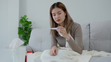 Young Asian woman having high fever while checking body temperature, female sneezing and runny nose with seasonal influenza, allergic, digital thermometer, virus, coronavirus, illness, respiratory