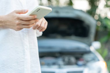 breakdown, broken car, repair. Woman uses mobile phone check insurance premiums through application due to car accident . Find garage to get car fixed during country tour, waiting for help, emergency.