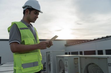 Asyalı bakım mühendisi fabrikanın çatısında çalışıyor. Müteahhit kompresör sistemini denetleyecek ve inşaatta havalandırma sistemi kurmayı planlıyor. Teknoloji, çevrimiçi kontrol