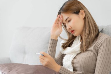 Young Asian woman having high fever while checking body temperature, female sneezing and runny nose with seasonal influenza, allergic, digital thermometer, virus, coronavirus, illness, respiratory