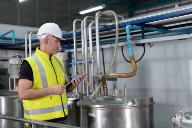 Güvenlik kaskı takan mühendisler veya fabrika yöneticileri üretim hattındaki makineleri inceler. Kamu müfettişi makineyi kontrol et ve standardı karşılamak için sistemi test et. makine, bakım.