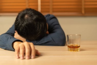 Depresyondaki genç Asyalı adam evde yalnız başına viski içmenin kötü hissettirdiğini vurguladı alkol içmek sorunlu içki, alkolizm, hayat ve aile sorunlarından muzdarip.