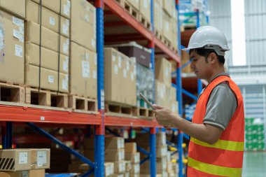 Asyalı erkek fabrikası depodaki malları ya da stok ürünlerini kontrol ediyor. Lojistik ticaret nakliyesi, müşterilere teslimat. Denetleme, depo, depo, fabrika