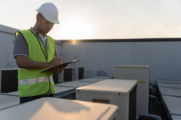 Asian maintenance engineer works on the roof of factory. contractor inspect compressor system and plans installation of air condition systems in construction. Checklist, inspector, control