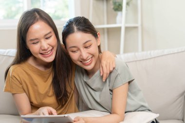 LGBT grubu. Güzel görünümlü lezbiyen çiftler tatilde evde tablet kullanır. Asyalı genç çift birbirlerine mutlu bir şekilde sarılıyorlar, aşık, biseksüellik, homoseksüellik, özgürlük, ifade, mutlu hayat.