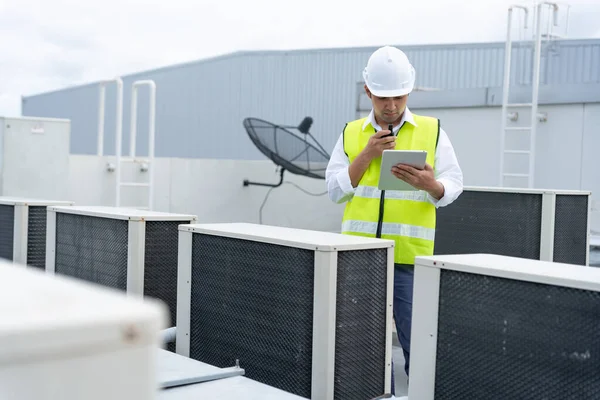 Asian maintenance engineer works on the roof of factory. contractor inspect compressor system and plans installation of air condition systems in construction. technology, online, mobile application.
