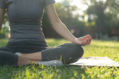 Kadın parkta meditasyon yapıyor. Sabahları egzersiz yapan Asyalı bir kadın. denge, dinlenme, rahatlama, sakinlik, sağlık, mutluluk, rahatlama, sağlıklı yaşam tarzı, stresi azaltma, huzur, tutum.