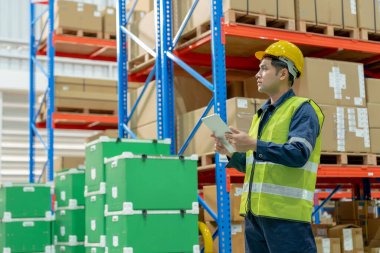 Asya 'daki erkek fabrika envanterini inceleyip kontrol ediyor, stok ürünlerini sayıyor. Lojistik ticaret nakliyesi, müşterilere teslimat. Denetleme, depo, depolama, fabrika, yönetme.
