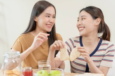 LGBT. Asyalı lezbiyen çift evde kahvaltı ederken gülümsüyor ve sevgi gösteriyor. Genç Asyalı çift birbirlerine mutlu bir şekilde sarılıyorlar, aşıklar, homoseksüellik, eşcinsellik, özgürlük, ifadeler.