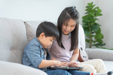 Küçük çocukla tablet kullanarak öğretmencilik oynayan mutlu bekar anne. Aile evde mutlu ve heyecanlı. Anne ve oğul birlikte vakit geçiriyorlar, iyi baba, bağımlılık düzelt, kontrol et, kontrol et.