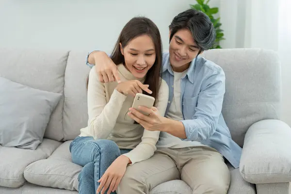 stock image Asian couple smiling and happily use smartphone to online shopping. Husband ready to pay birthday present for beautiful wife. Find accommodation online for honeymoon, App online, book flight tickets.