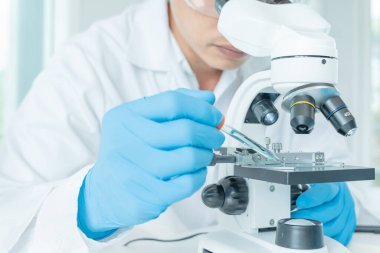 Bilimadamı ileri bilimsel laboratuvarda biyokimyasal örnekleri analiz ediyor. Tıbbi profesyonel kullanım mikroskobu virüsün mikrobiyolojik gelişimini gösteriyor. Fen laboratuvarında biyoteknoloji araştırması.