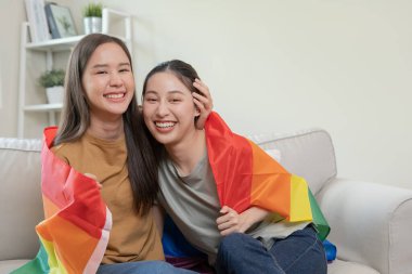 LGBT grubu. Güzel görünümlü lezbiyen çiftler gökkuşağı bayraklarını parlak bir şekilde örterler. Asyalı genç çift birbirlerine mutlu bir şekilde sarılıyorlar, aşık olan sevgili, biseksüeller, homoseksüellik, özgürlük, ifade, mutlu hayat.