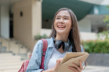 Sırt çantası ve kitapları açık havada olan Asyalı güzel bir öğrenci. Üniversite kampüsünde kitap taşımaktan mutlu gülümseyen kız. Uluslararası Asya Üniversitesi 'nde kadın portresi. Eğitim, eğitim, okul