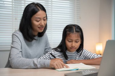 Anne, kızına dizüstü bilgisayardan ders veriyor. Asyalı küçük kız evde öğreniyor. Nazik anneyle ödev yap, sınav için cesaretlendir. Asyalı kız mutlu bir ev okulu. Annem birlikte eğitim veriyor..