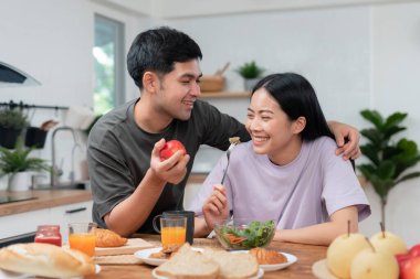 Asyalı çiftler yeni evlerinin tadını çıkarıyor ve birlikte kahvaltı ediyorlar. Karı koca evlendikten sonra. Sıcak bir ailede mutluluk, gülümseme ve kahkaha. Sarılma, sıcak sarılmalar, mutlu aile ve mutlu bir gün.