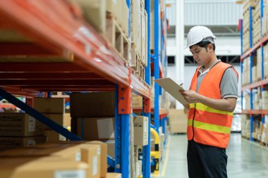 Asya 'daki erkek fabrika envanterini inceleyip kontrol ediyor, stok ürünlerini sayıyor. Lojistik ticaret nakliyesi, müşterilere teslimat. Denetleme, depo, depolama, fabrika, yönetme.