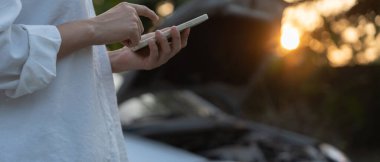 breakdown, broken car, repair. Woman uses mobile phone check insurance premiums through application due to car accident . Find garage to get car fixed during country tour, waiting for help, emergency.