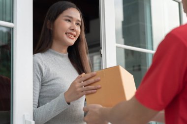 Mutlu gülümseyen Asyalı kadın, kurye evinden karton kutu yiyecek alıyor. Teslimatçı ekspres teslimat gönderdi. Çevrimiçi alışveriş, kağıt konteynır, paket servisi, postacı, dağıtım servisi, paketler