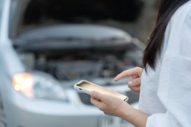 breakdown, broken car, repair. Woman uses mobile phone check insurance premiums through application due to car accident . Find garage to get car fixed during country tour, waiting for help, emergency.