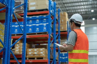 Asya 'daki erkek fabrika envanterini inceleyip kontrol ediyor, stok ürünlerini sayıyor. Lojistik ticaret nakliyesi, müşterilere teslimat. Denetleme, depo, depolama, fabrika, yönetme.