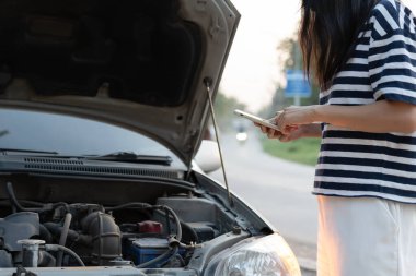 breakdown, broken car, repair. Woman uses mobile phone check insurance premiums through application due to car accident . Find garage to get car fixed during country tour, waiting for help, emergency.