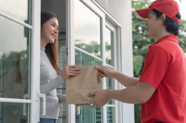 Mutlu gülümseyen Asyalı kadın, kurye evinden bir paket yiyecek alıyor. Teslimatçı ekspres teslimat gönderdi. Çevrimiçi alışveriş, kağıt konteynır, paket servisi, postacı, dağıtım servisi, paketler