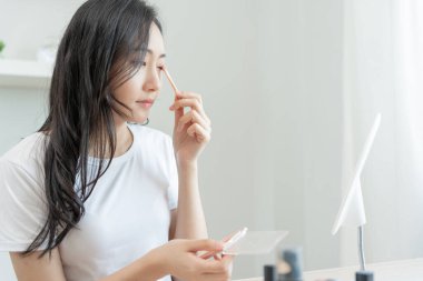 Güzel bir Asyalı kadın aynanın önünde oturur. Makyaj yapan sağlıklı bir kadının yüzü. Cilt bakımı, kırışıklık önleyici, bebek yüzü, beyazlatma, nemlendirici, gözenekleri sıkılaştırma serumu.