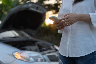 breakdown, broken car, repair. Woman uses mobile phone check insurance premiums through application due to car accident . Find garage to get car fixed during country tour, waiting for help, emergency.