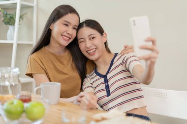 LGBT grubu. Güzel görünümlü lezbiyen çiftler tatilde evde tablet kullanır. Asyalı genç çift birbirlerine mutlu bir şekilde sarılıyorlar, aşık, biseksüellik, homoseksüellik, özgürlük, ifade, mutlu hayat.
