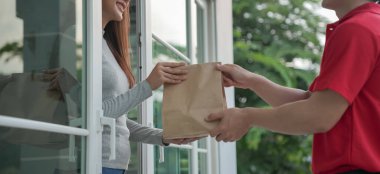 Mutlu gülümseyen Asyalı kadın, kurye evinden bir paket yiyecek alıyor. Teslimatçı ekspres teslimat gönderdi. Çevrimiçi alışveriş, kağıt konteynır, paket servisi, postacı, dağıtım servisi, paketler