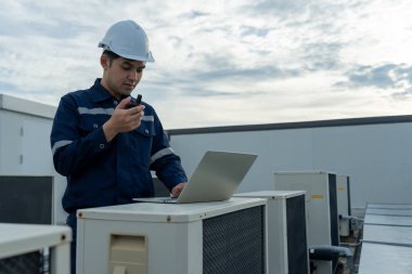 Asian maintenance engineer work on the roof of factory. contractor inspect compressor system and plans installation of air condition systems in construction. technology, walky talky, maintenance