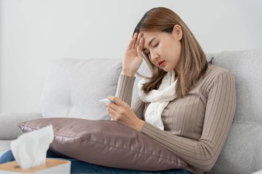 Young Asian woman having high fever while checking body temperature, female sneezing and runny nose with seasonal influenza, allergic, digital thermometer, virus, coronavirus, illness, respiratory