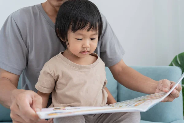 father relax and read book with baby time together at home. parent sit on sofa with daughter and reading a story. learn development, childcare, laughing, education, storytelling, practice.