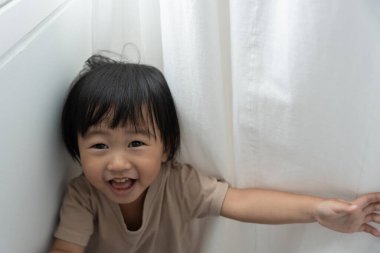 Küçük Asyalı çocuk, duvar evinde saklambaç oynuyor, sevimli çocuk evde eğleniyor. Mutlu aile çocuklarla, aktivitelerle, öğrenmeyle eğlenir.