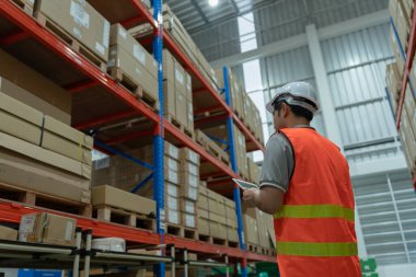 Asya 'daki erkek fabrika envanterini inceleyip kontrol ediyor, stok ürünlerini sayıyor. Lojistik ticaret nakliyesi, müşterilere teslimat. Denetleme, depo, depolama, fabrika, yönetme.